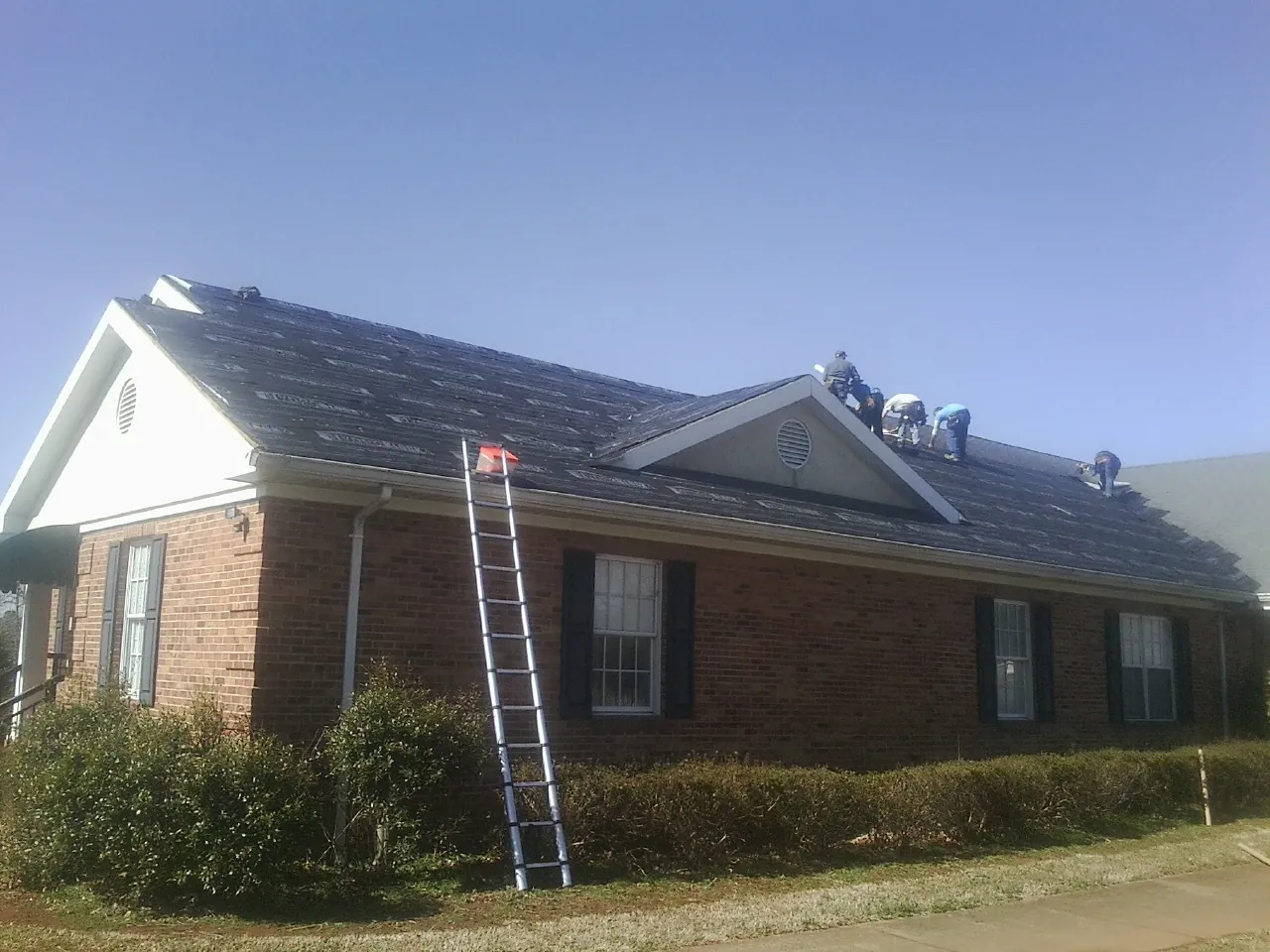 Crew tearing shingles off a brick ranch roof with a ladder set — Emergency Roof Repair work by our crew in Whitwell
