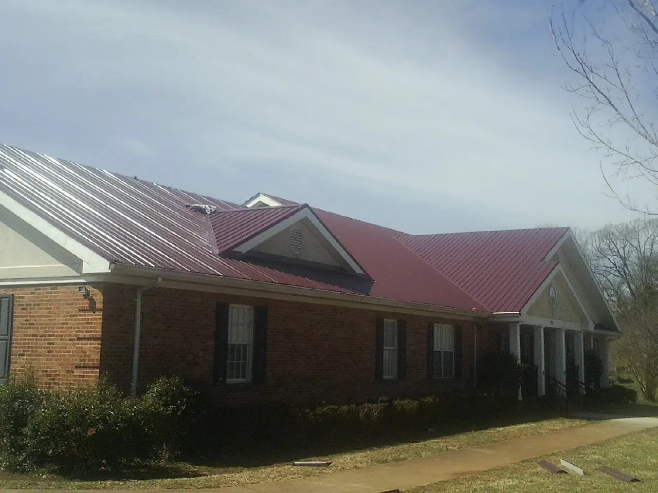 Red metal roof with gabled entries on a long brick building, from a Hail Damage Roof Repair job in Whitwell