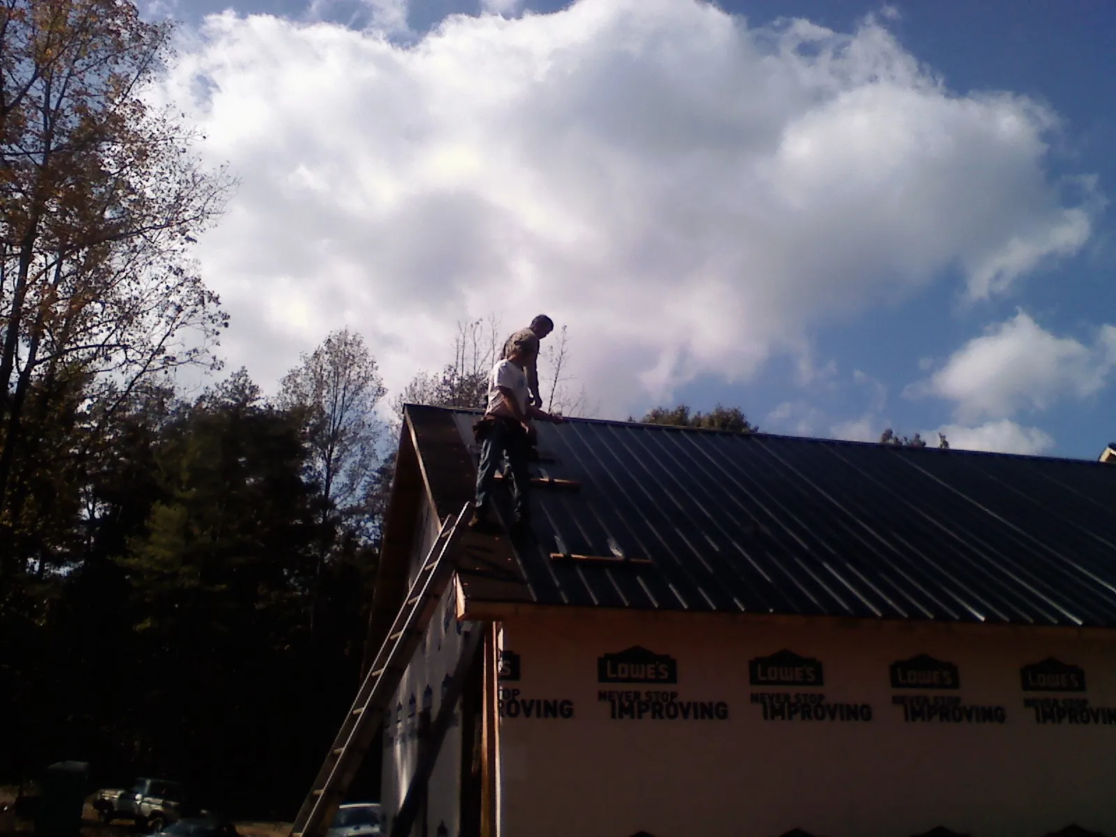 Roofer fastening dark metal panels high against a cloudy sky, from a Roof Inspection job in Whitwell