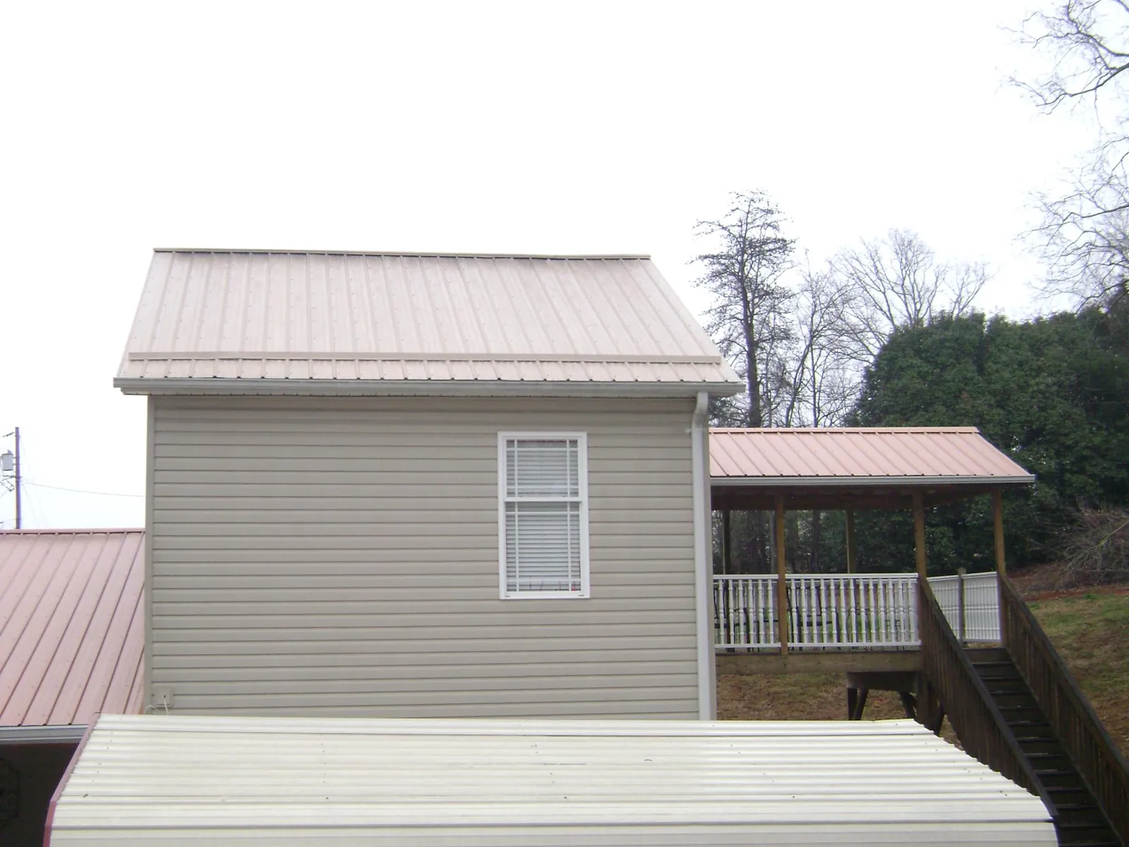 Tan metal roofs on a two story addition and attached porch, from a Roof Replacement job in Whitwell